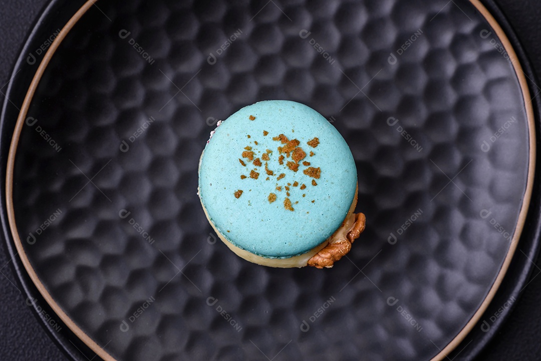 Lindo macaron saboroso com recheio e sabor de frutas em uma placa preta sobre um fundo escuro de concreto