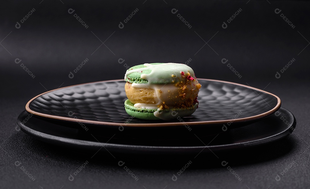 Lindo macaron saboroso com recheio e sabor de frutas em uma placa preta sobre um fundo escuro de concreto