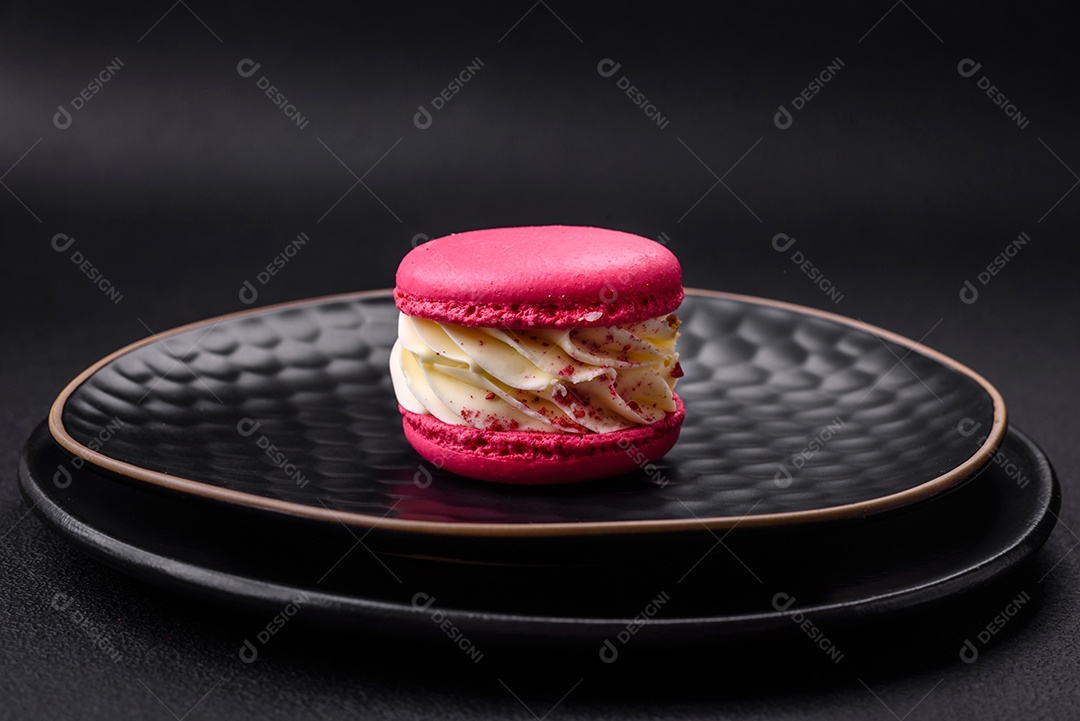 Lindo macaron saboroso com recheio e sabor de frutas em uma placa preta sobre um fundo escuro de concreto