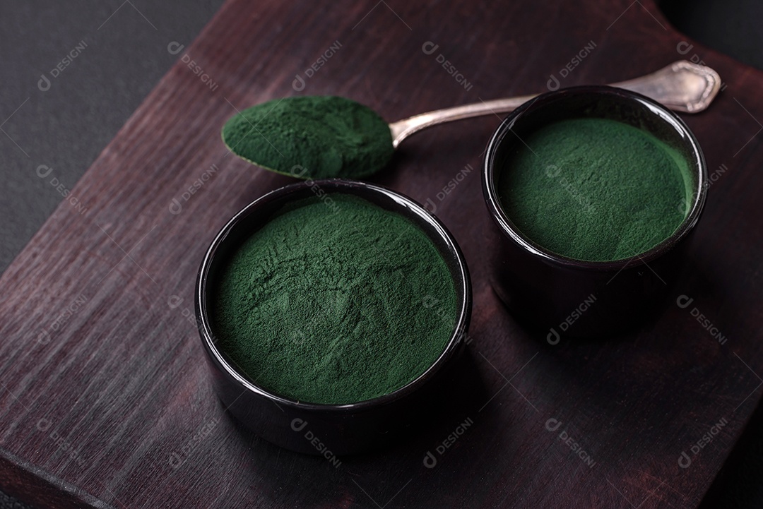 Especiaria, espirulina de cor verde em forma de pó em uma tigela preta sobre um fundo escuro de concreto