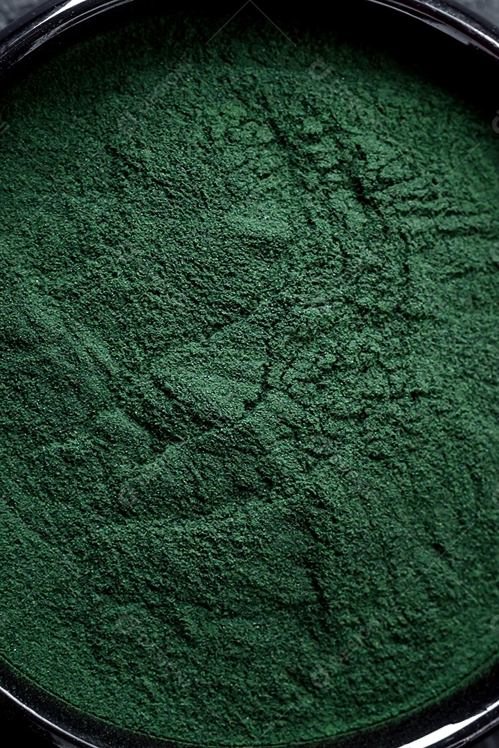 Especiaria, espirulina de cor verde em forma de pó em uma tigela preta sobre um fundo escuro de concreto
