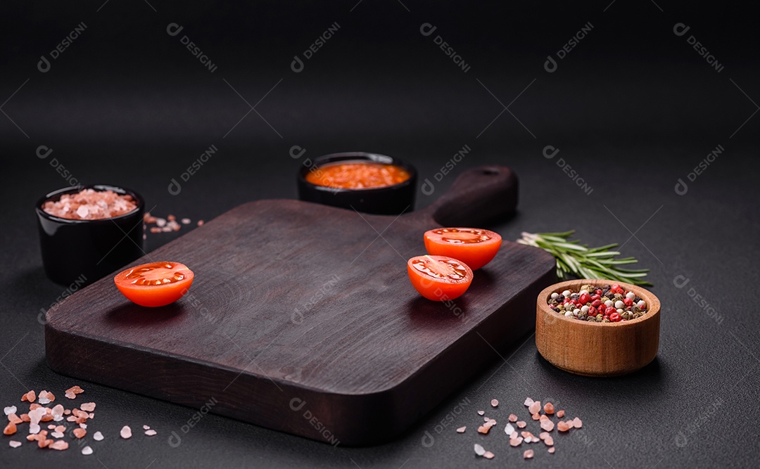 Tábua de madeira com legumes, especiarias e ervas sobre um fundo escuro de concreto