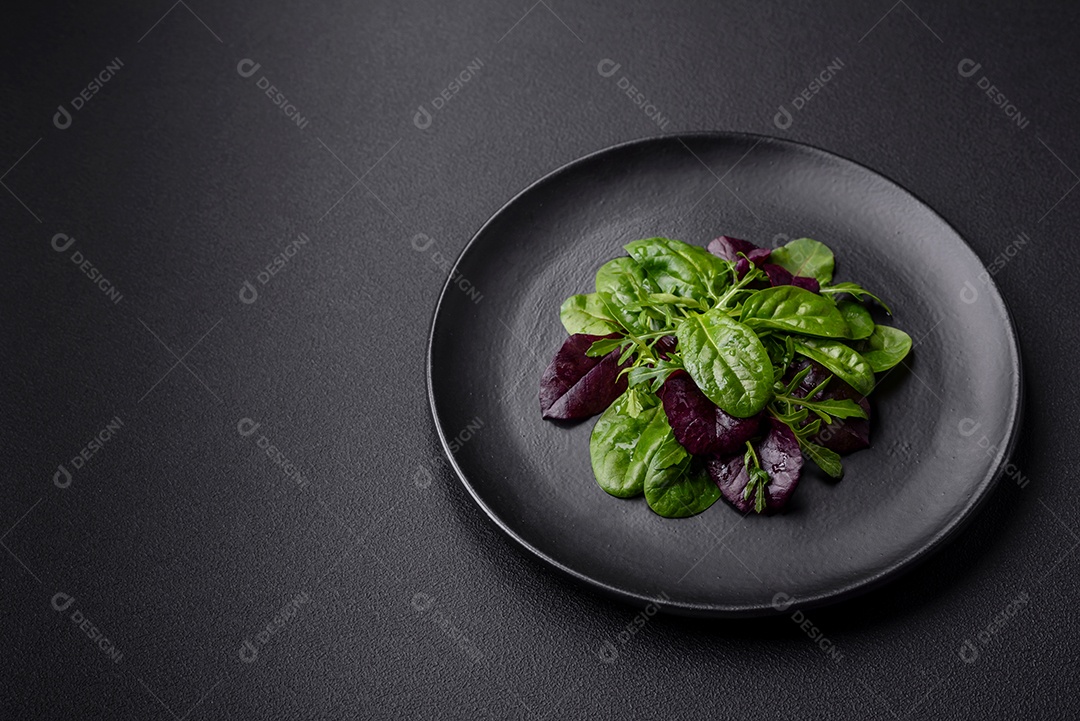 Deliciosa salada fresca composta por espinafre, acelga, radicchio, gráfico vermelho, sangue de touros e rúcula em uma placa preta sobre um fundo escuro de concreto