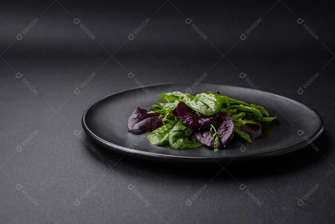 Deliciosa salada fresca composta por espinafre, acelga, radicchio, gráfico vermelho, sangue de touros e rúcula em uma placa preta sobre um fundo escuro de concreto