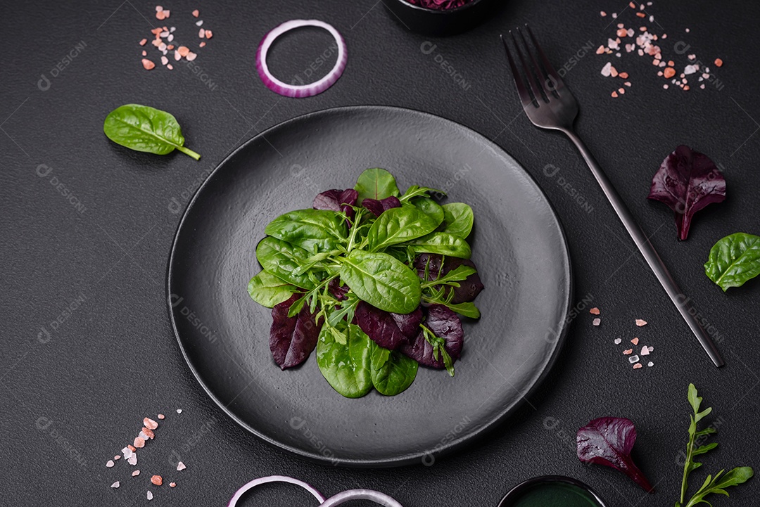 Deliciosa salada fresca composta por espinafre, acelga, radicchio, gráfico vermelho, sangue de touros e rúcula em uma placa preta sobre um fundo escuro de concreto
