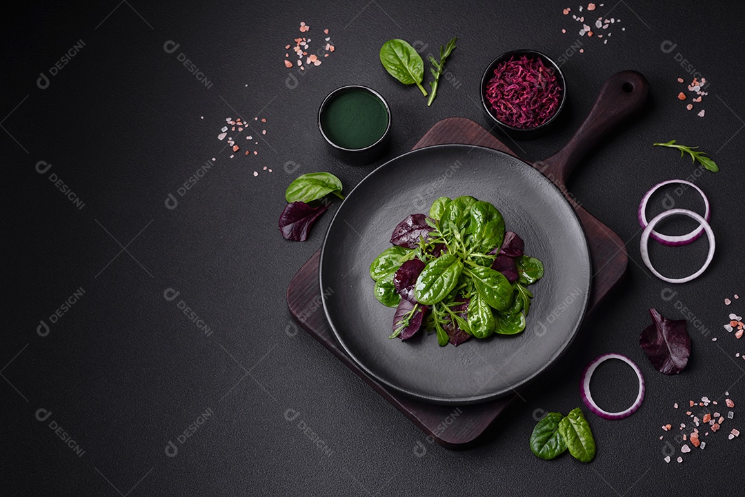 Deliciosa salada fresca composta por espinafre, acelga, radicchio, gráfico vermelho, sangue de touros e rúcula em uma placa preta sobre um fundo escuro de concreto