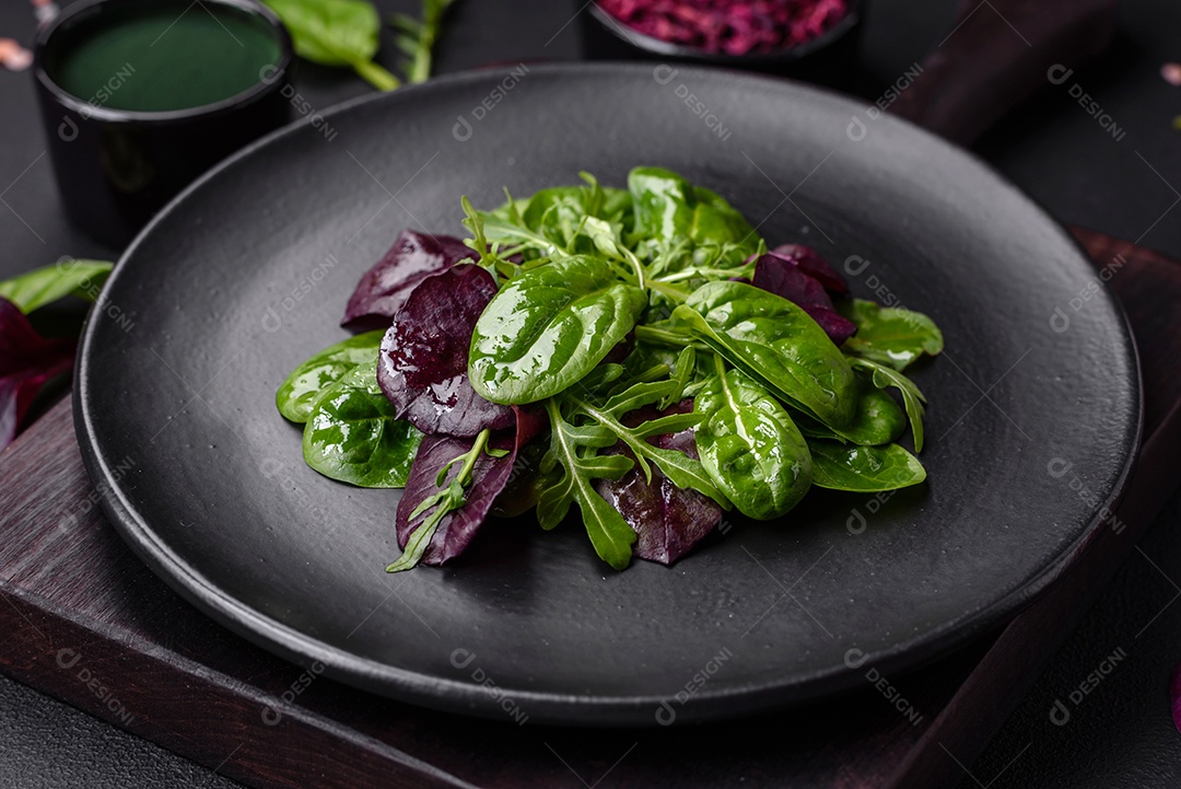 Deliciosa salada fresca composta por espinafre, acelga, radicchio, gráfico vermelho, sangue de touros e rúcula em uma placa preta sobre um fundo escuro de concreto