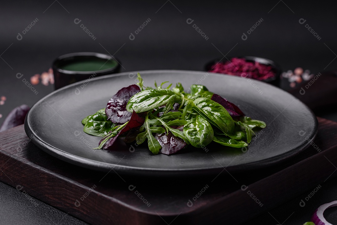 Deliciosa salada fresca composta por espinafre, acelga, radicchio, gráfico vermelho, sangue de touros e rúcula em uma placa preta sobre um fundo escuro de concreto