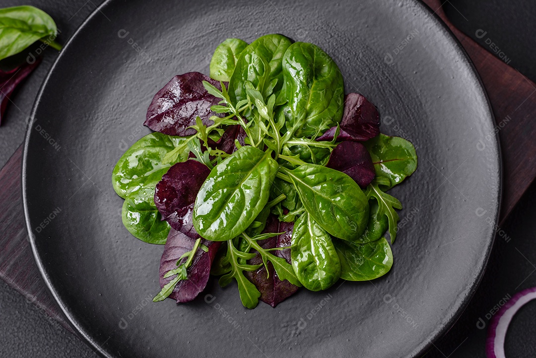 Deliciosa salada fresca composta por espinafre, acelga, radicchio, gráfico vermelho, sangue de touros e rúcula em uma placa preta sobre um fundo escuro de concreto