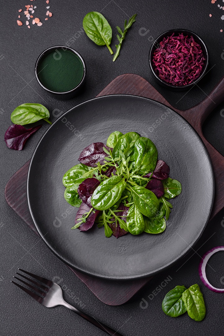 Deliciosa salada fresca composta por espinafre, acelga, radicchio, gráfico vermelho, sangue de touros e rúcula em uma placa preta sobre um fundo escuro de concreto