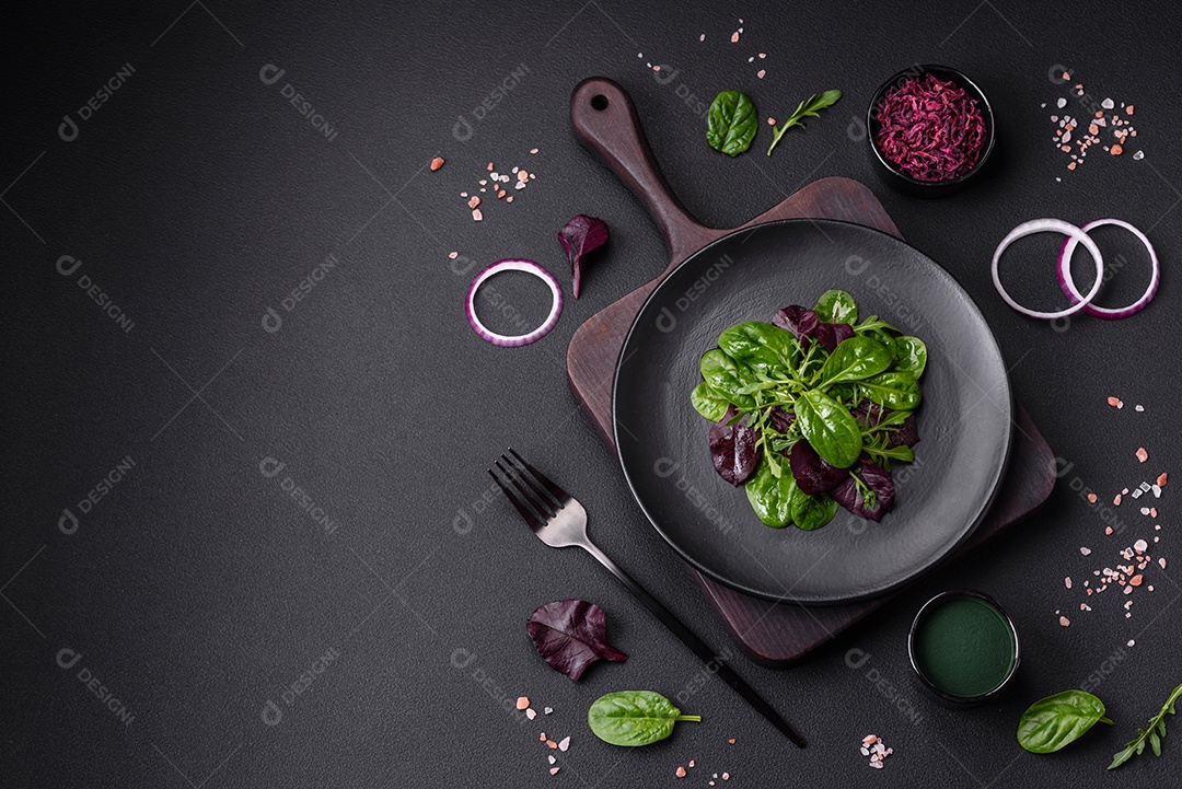 Deliciosa salada fresca composta por espinafre, acelga, radicchio, gráfico vermelho, sangue de touros e rúcula em uma placa preta sobre um fundo escuro de concreto