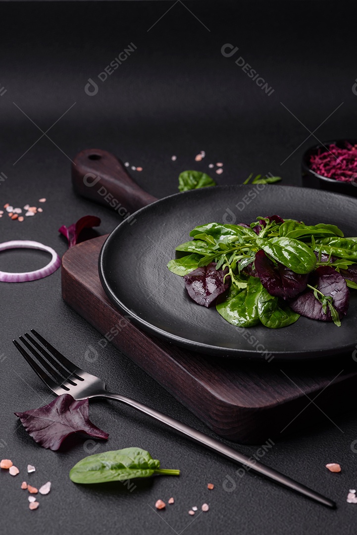 Deliciosa salada fresca composta por espinafre, acelga, radicchio, gráfico vermelho, sangue de touros e rúcula em uma placa preta sobre um fundo escuro de concreto