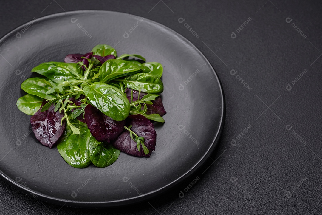 Deliciosa salada fresca composta por espinafre, acelga, radicchio, gráfico vermelho, sangue de touros e rúcula em uma placa preta sobre um fundo escuro de concreto