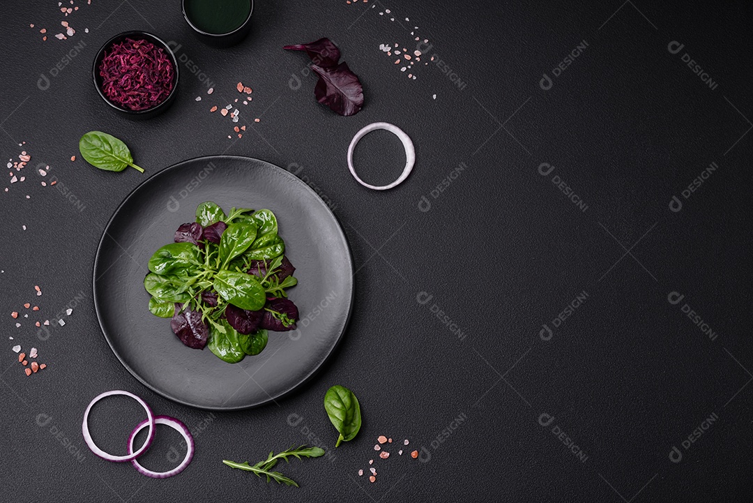 Deliciosa salada fresca composta por espinafre, acelga, radicchio, gráfico vermelho, sangue de touros e rúcula em uma placa preta sobre um fundo escuro de concreto