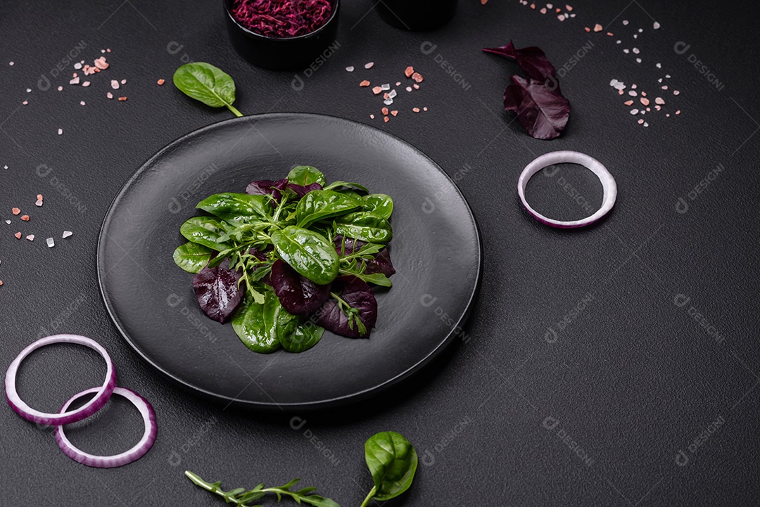 Deliciosa salada fresca composta por espinafre, acelga, radicchio, gráfico vermelho, sangue de touros e rúcula em uma placa preta sobre um fundo escuro de concreto