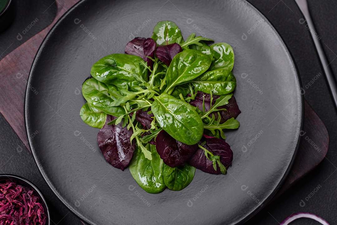 Deliciosa salada fresca composta por espinafre, acelga, radicchio, gráfico vermelho, sangue de touros e rúcula em uma placa preta sobre um fundo escuro de concreto