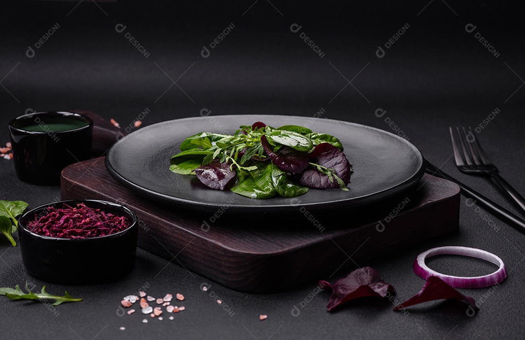 Deliciosa salada fresca composta por espinafre, acelga, radicchio, gráfico vermelho, sangue de touros e rúcula em uma placa preta sobre um fundo escuro de concreto