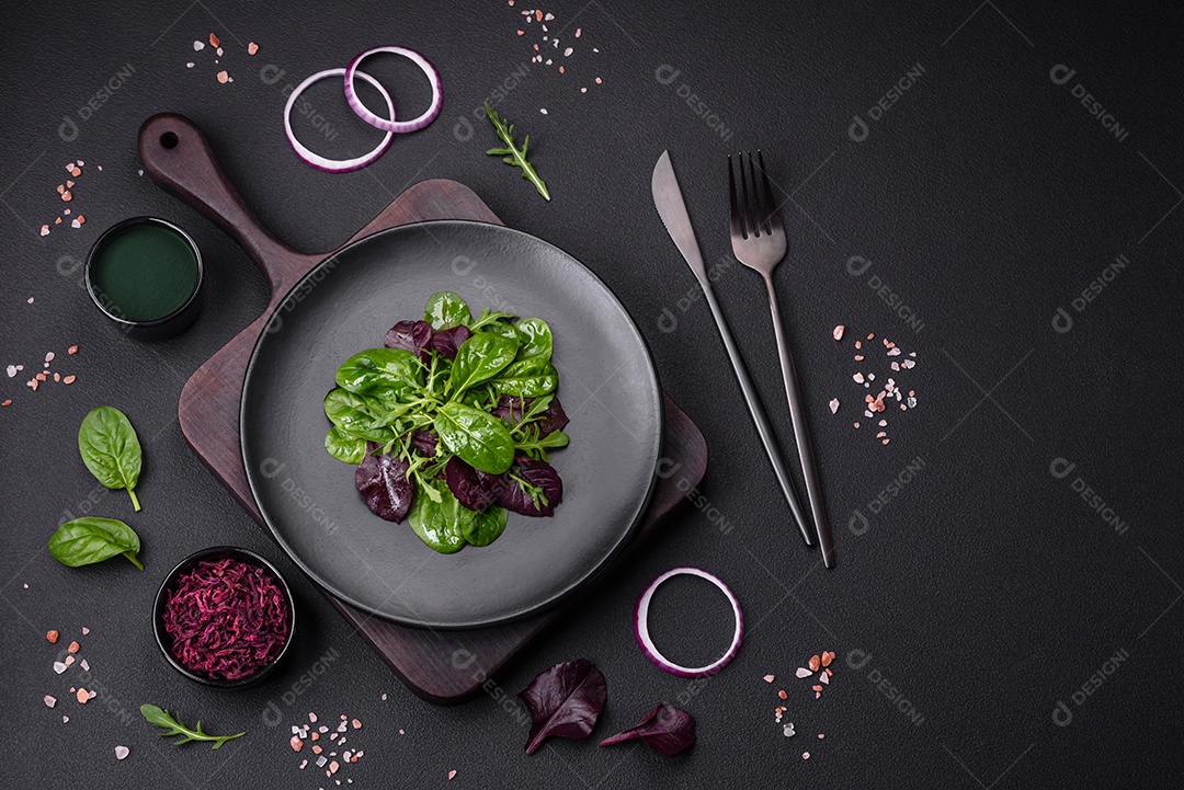 Deliciosa salada fresca composta por espinafre, acelga, radicchio, gráfico vermelho, sangue de touros e rúcula em uma placa preta sobre um fundo escuro de concreto