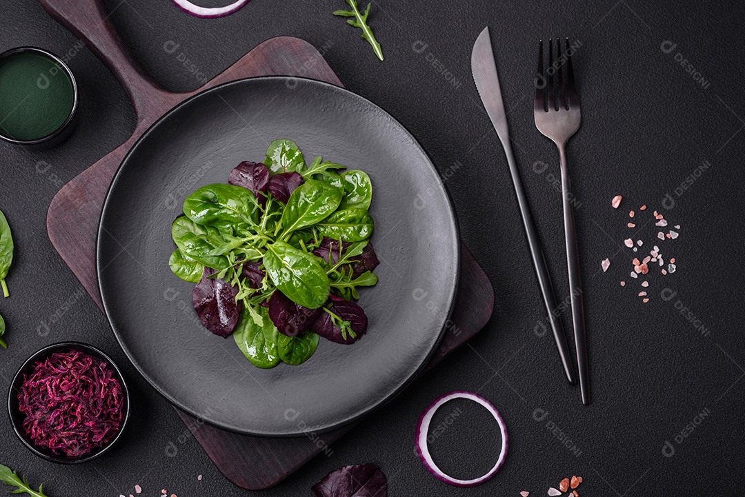 Deliciosa salada fresca composta por espinafre, acelga, radicchio, gráfico vermelho, sangue de touros e rúcula em uma placa preta sobre um fundo escuro de concreto