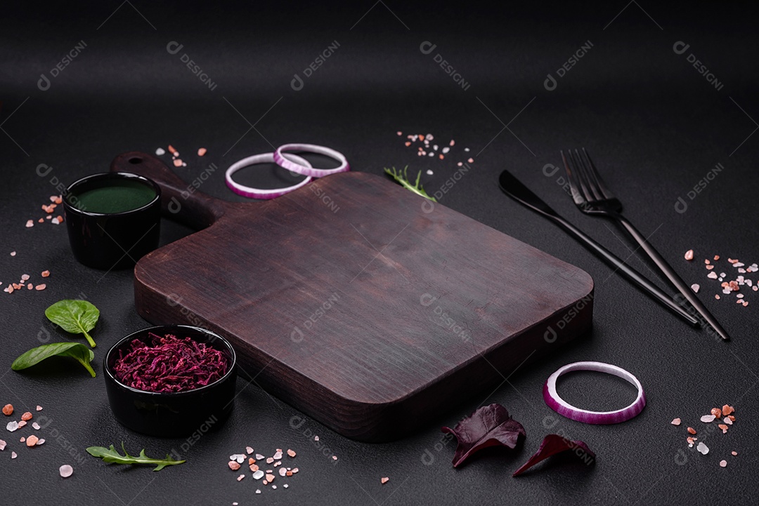 Deliciosa salada fresca composta por espinafre, acelga, radicchio, gráfico vermelho, sangue de touros e rúcula em uma placa preta sobre um fundo escuro de concreto