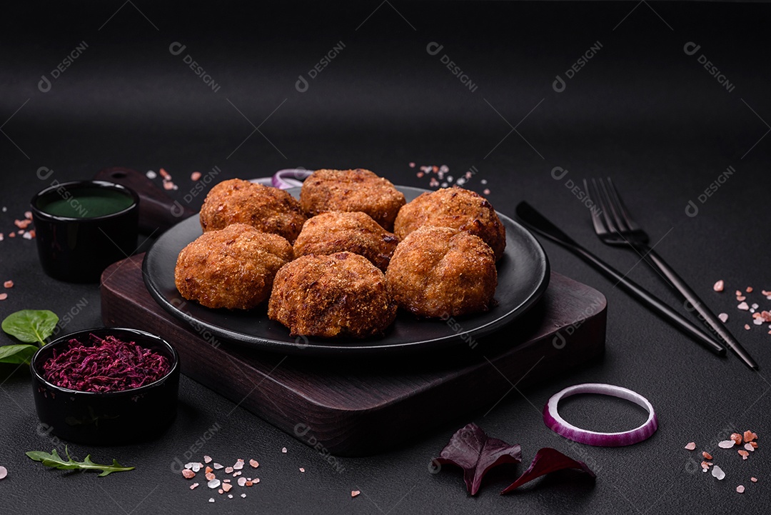 Deliciosas costeletas de carne fresca ou vegetais com especiarias e ervas em uma placa preta sobre um fundo escuro de concreto