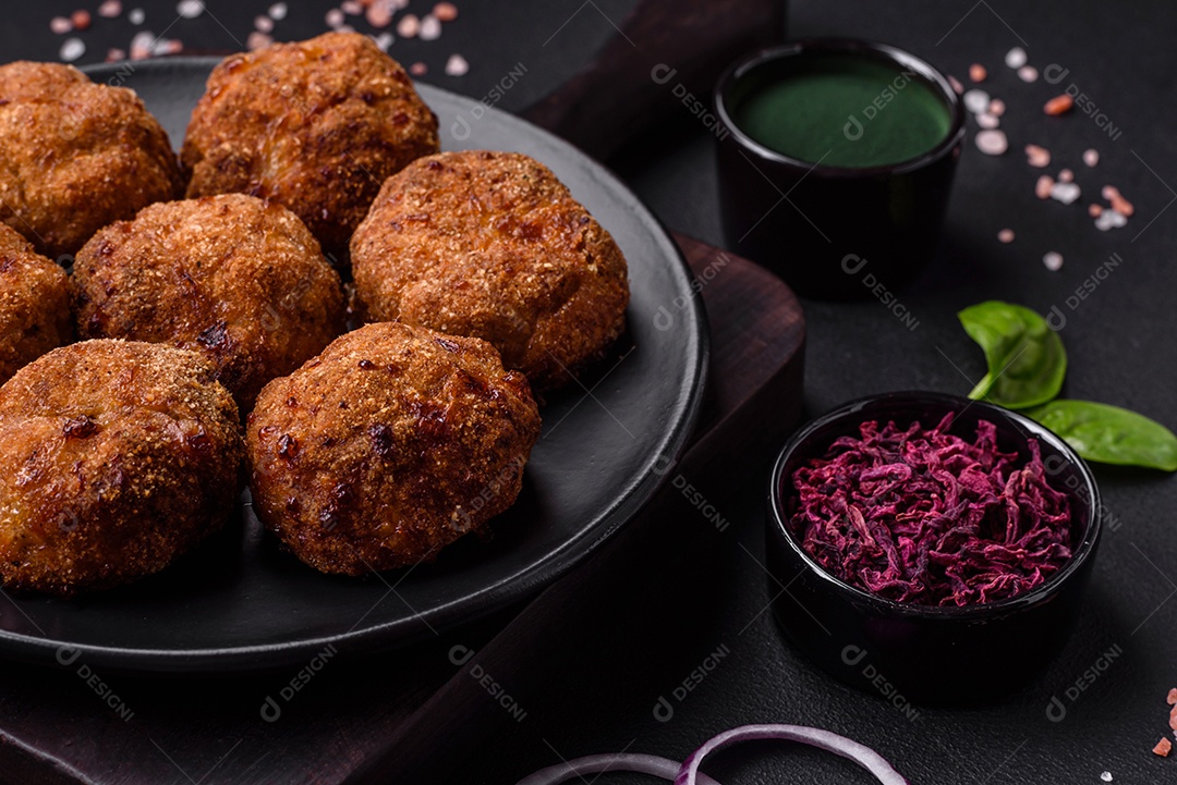 Deliciosas costeletas de carne fresca ou vegetais com especiarias e ervas em uma placa preta sobre um fundo escuro de concreto