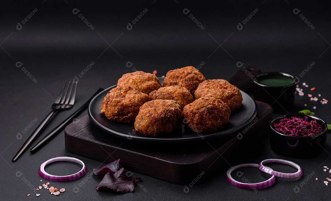 Deliciosas costeletas de carne fresca ou vegetais com especiarias e ervas em uma placa preta sobre um fundo escuro de concreto