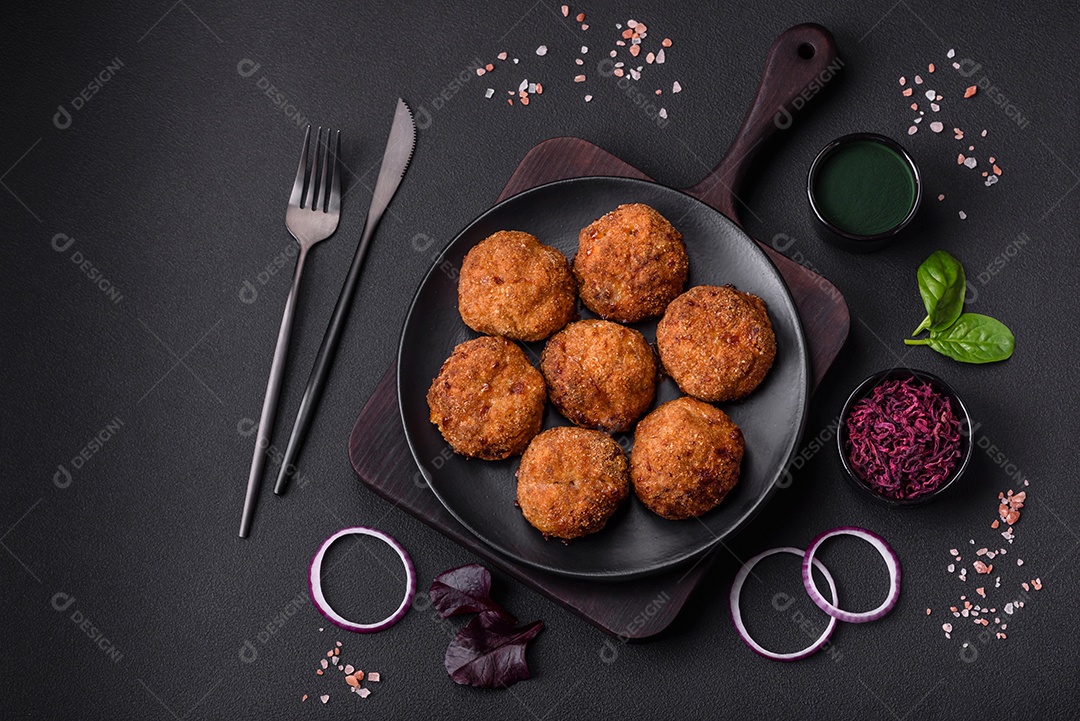 Deliciosas costeletas de carne fresca ou vegetais com especiarias e ervas em uma placa preta sobre um fundo escuro de concreto