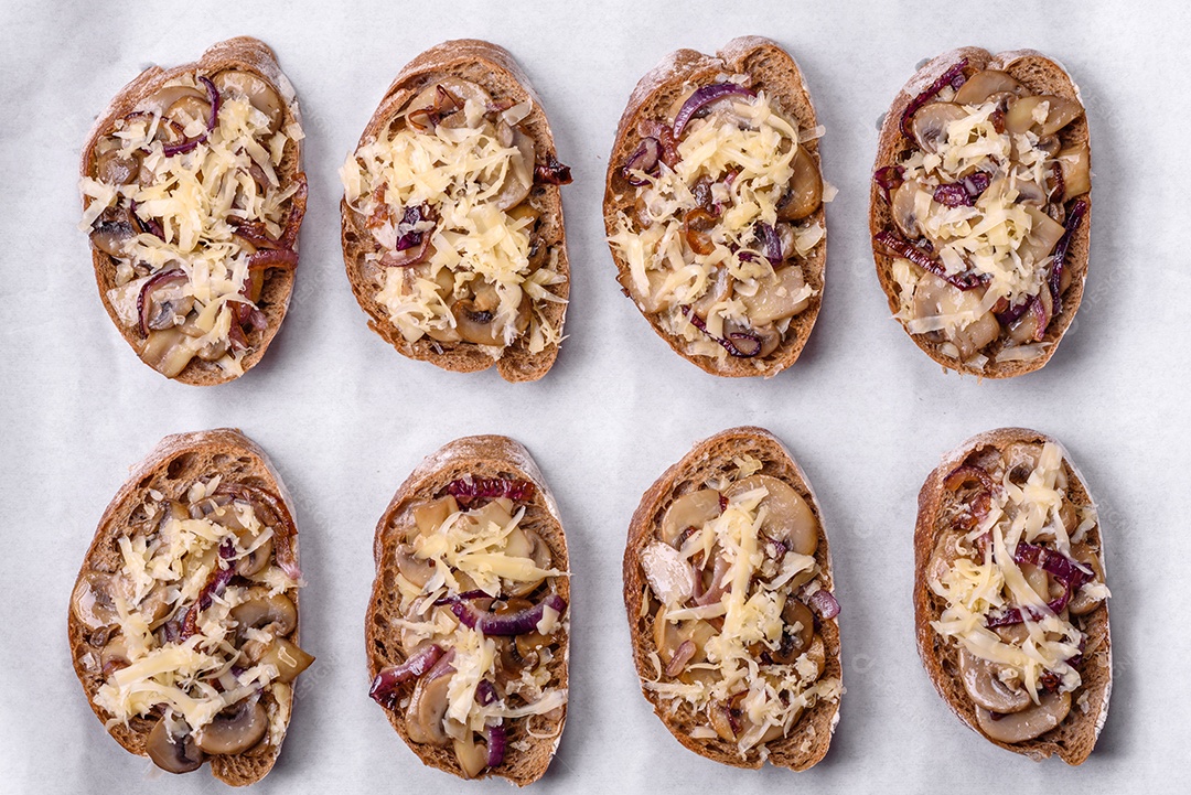 Deliciosa torrada crocante ou bruscheta com cebola frita, cogumelos champignon e queijo com especiarias e ervas sobre um fundo escuro de concreto