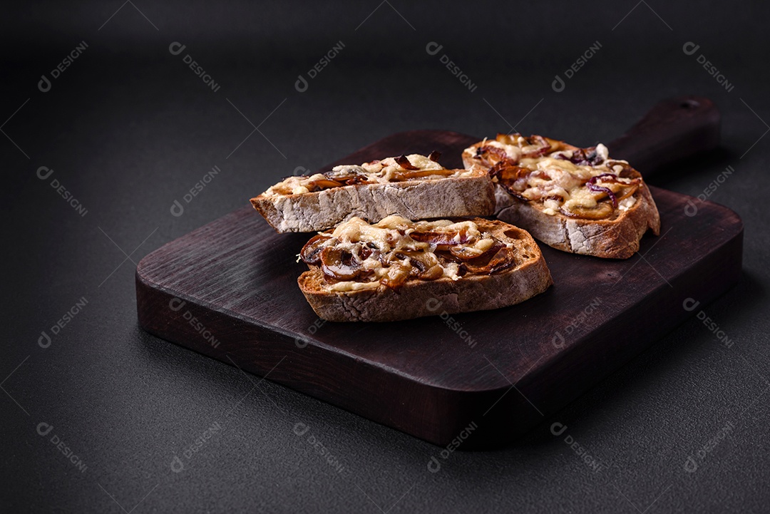 Deliciosa torrada crocante ou bruscheta com cebola frita, cogumelos champignon e queijo com especiarias e ervas sobre um fundo escuro de concreto