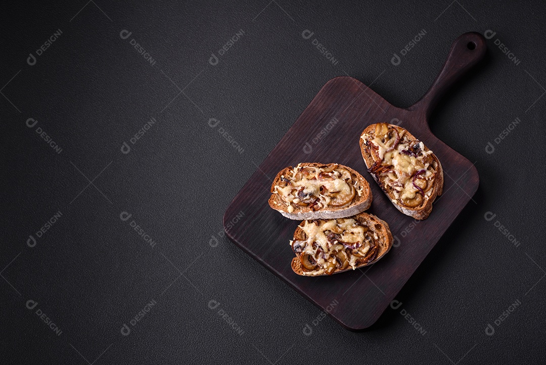 Deliciosa torrada crocante ou bruscheta com cebola frita, cogumelos champignon e queijo com especiarias e ervas sobre um fundo escuro de concreto