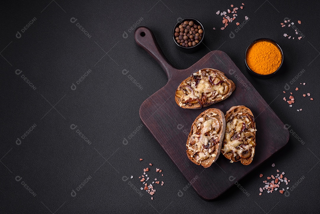 Deliciosa torrada crocante ou bruscheta com cebola frita, cogumelos champignon e queijo com especiarias e ervas sobre um fundo escuro de concreto