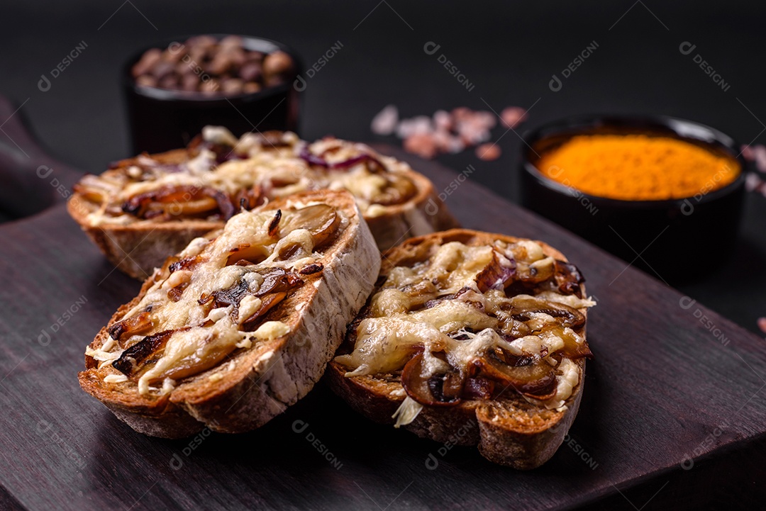 Deliciosa torrada crocante ou bruscheta com cebola frita, cogumelos champignon e queijo com especiarias e ervas sobre um fundo escuro de concreto