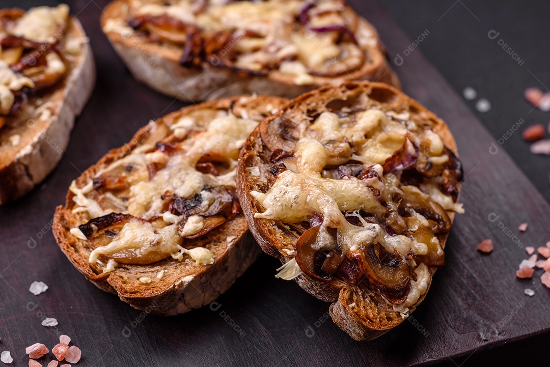 Deliciosa torrada crocante ou bruscheta com cebola frita, cogumelos champignon e queijo com especiarias e ervas sobre um fundo escuro de concreto