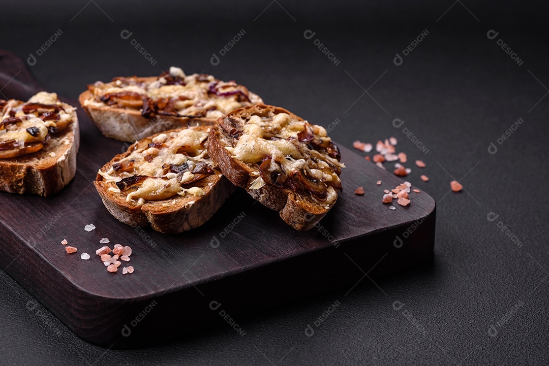 Deliciosa torrada crocante ou bruscheta com cebola frita, cogumelos champignon e queijo com especiarias e ervas sobre um fundo escuro de concreto