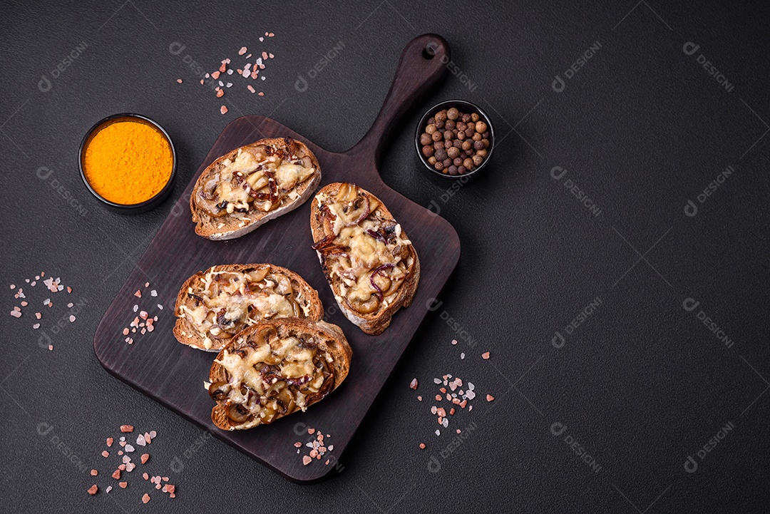 Deliciosa torrada crocante ou bruscheta com cebola frita, cogumelos champignon e queijo com especiarias e ervas sobre um fundo escuro de concreto