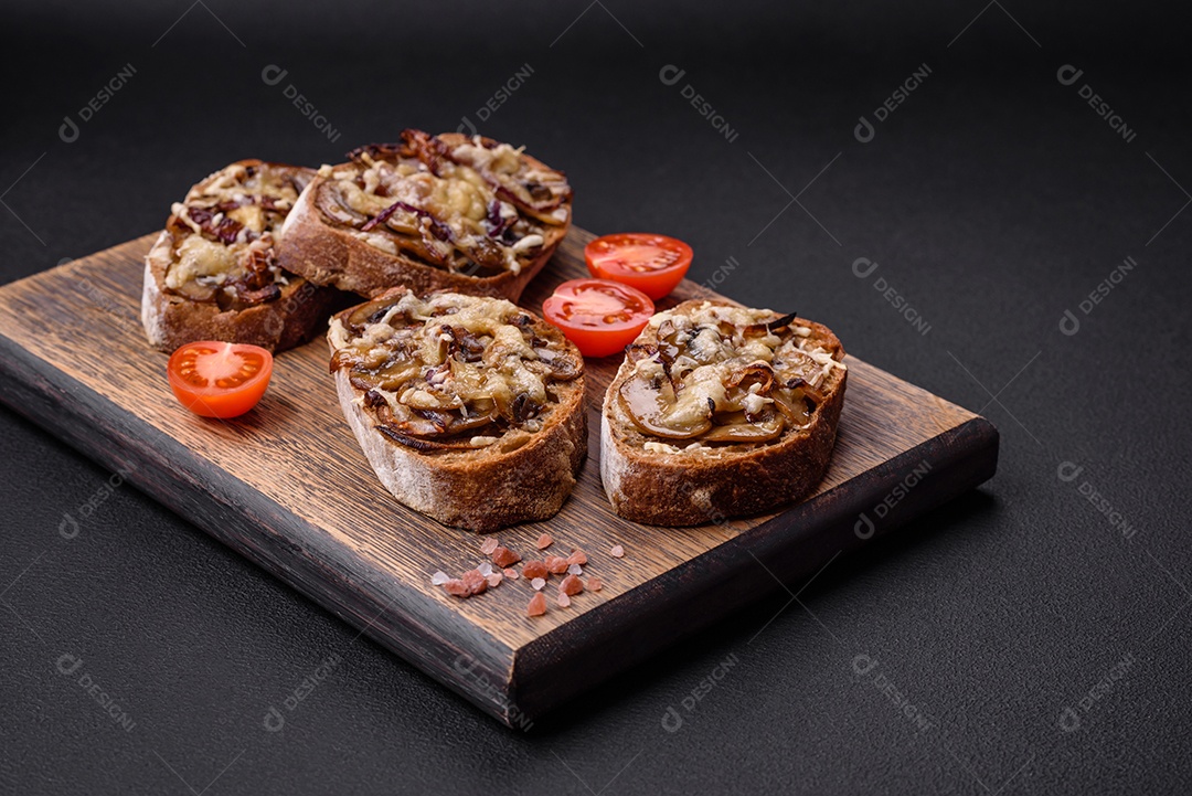 Deliciosa torrada crocante ou bruscheta com cebola frita, cogumelos champignon e queijo com especiarias e ervas sobre um fundo escuro de concreto