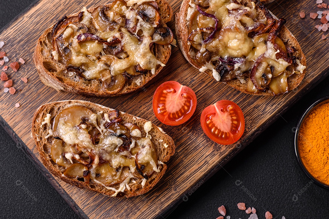 Deliciosa torrada crocante ou bruscheta com cebola frita, cogumelos champignon e queijo com especiarias e ervas sobre um fundo escuro de concreto