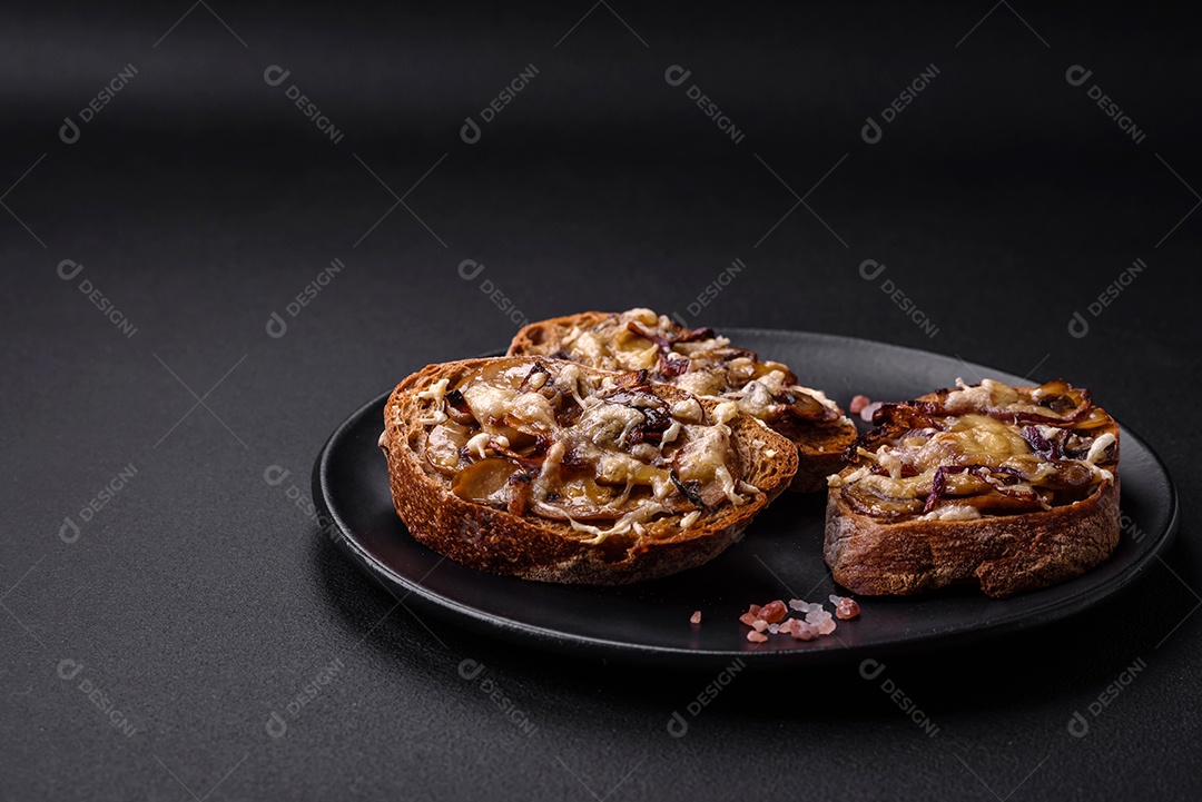 Deliciosa torrada crocante ou bruscheta com cebola frita, cogumelos champignon e queijo com especiarias e ervas sobre um fundo escuro de concreto