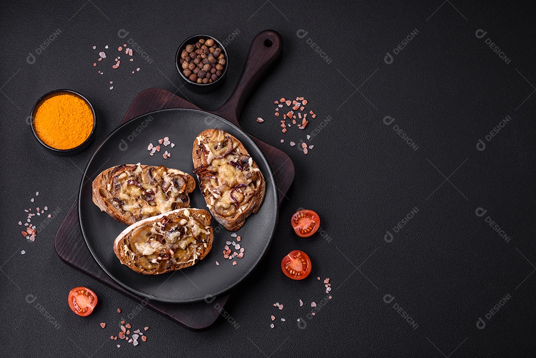 Deliciosa torrada crocante ou bruscheta com cebola frita, cogumelos champignon e queijo com especiarias e ervas sobre um fundo escuro de concreto