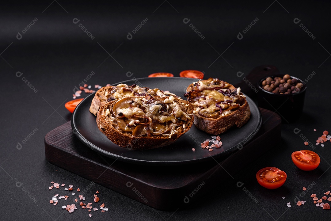 Deliciosa torrada crocante ou bruscheta com cebola frita, cogumelos champignon e queijo com especiarias e ervas sobre um fundo escuro de concreto