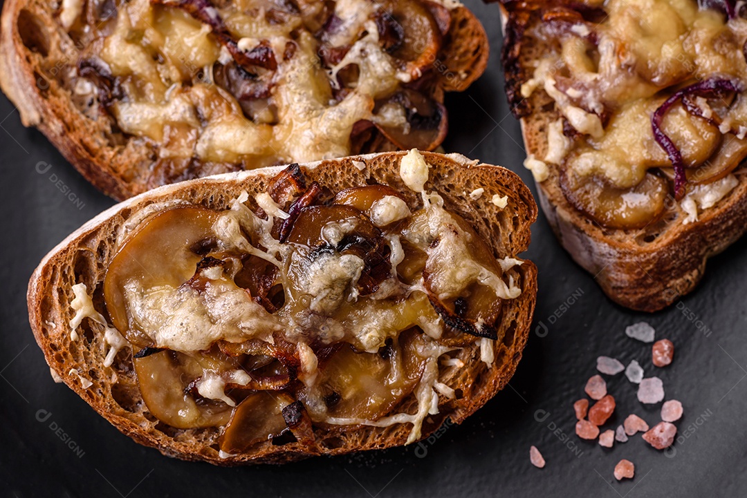 Deliciosa torrada crocante ou bruscheta com cebola frita, cogumelos champignon e queijo com especiarias e ervas sobre um fundo escuro de concreto