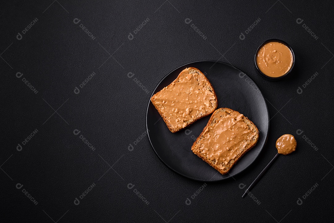 Sanduíche nutritivo composto por pão e manteiga de amendoim em uma placa de cerâmica preta sobre um fundo escuro de concreto