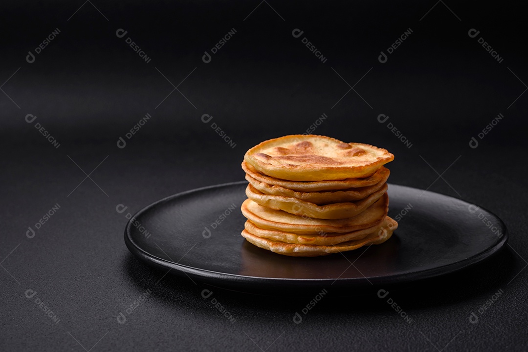 Deliciosas panquecas frescas com geléia de frutas vermelhas em uma placa de cerâmica preta sobre um fundo escuro de concreto