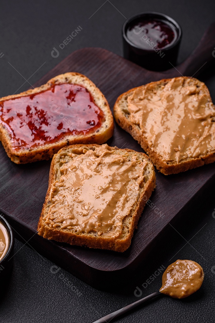 Sanduíches nutritivos compostos por pão, geléia de framboesa e manteiga de amendoim em uma placa de cerâmica preta sobre fundo escuro de concreto