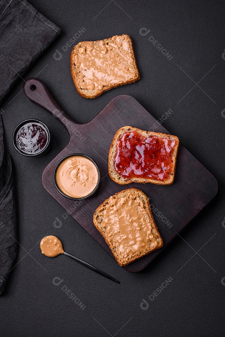 Sanduíches nutritivos compostos por pão, geléia de framboesa e manteiga de amendoim em uma placa de cerâmica preta sobre fundo escuro de concreto