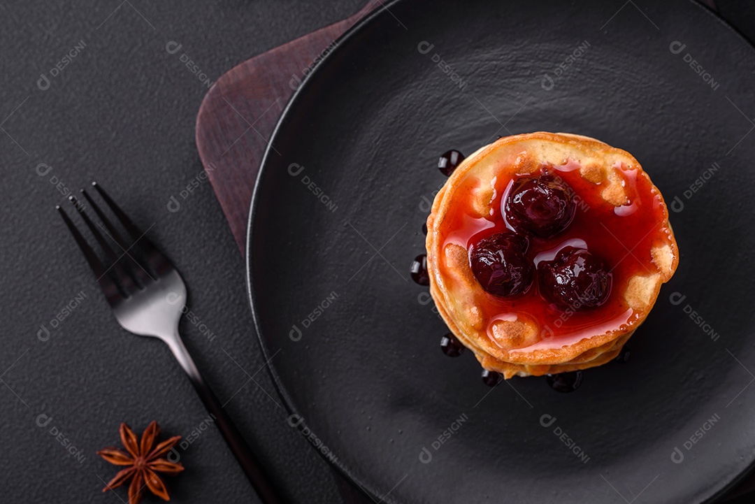 Deliciosas panquecas frescas com geléia de frutas vermelhas em uma placa de cerâmica preta sobre um fundo escuro de concreto