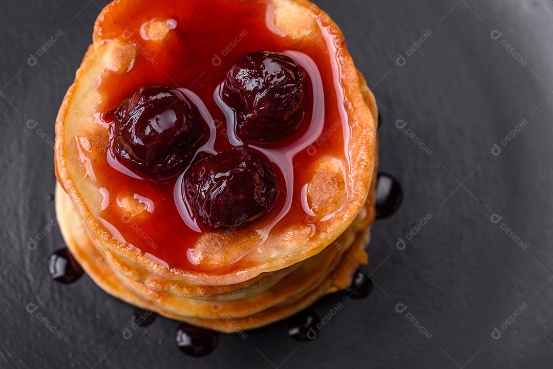 Deliciosas panquecas frescas com geléia de frutas vermelhas em uma placa de cerâmica preta sobre um fundo escuro de concreto