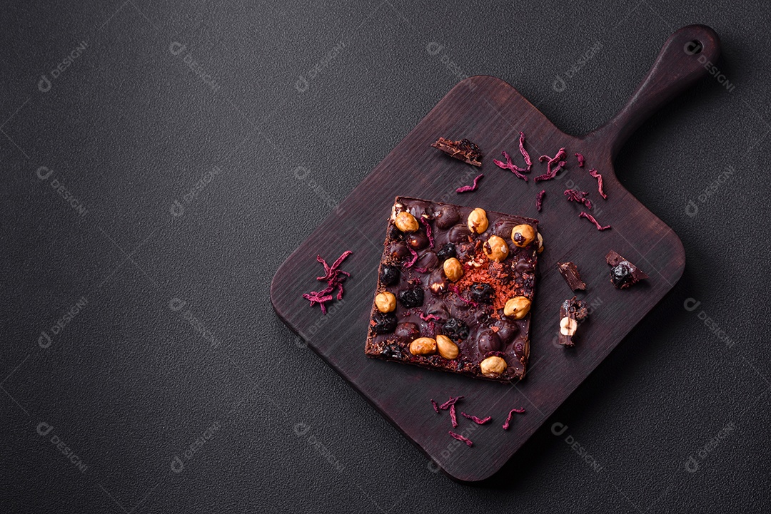 Chocolate artesanal com frutas, nozes e especiarias em um fundo escuro de concreto. Doces feitos em casa