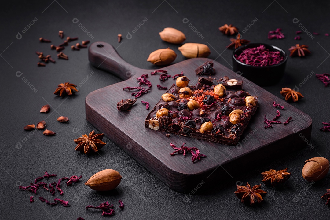 Chocolate artesanal com frutas, nozes e especiarias em um fundo escuro de concreto. Doces feitos em casa